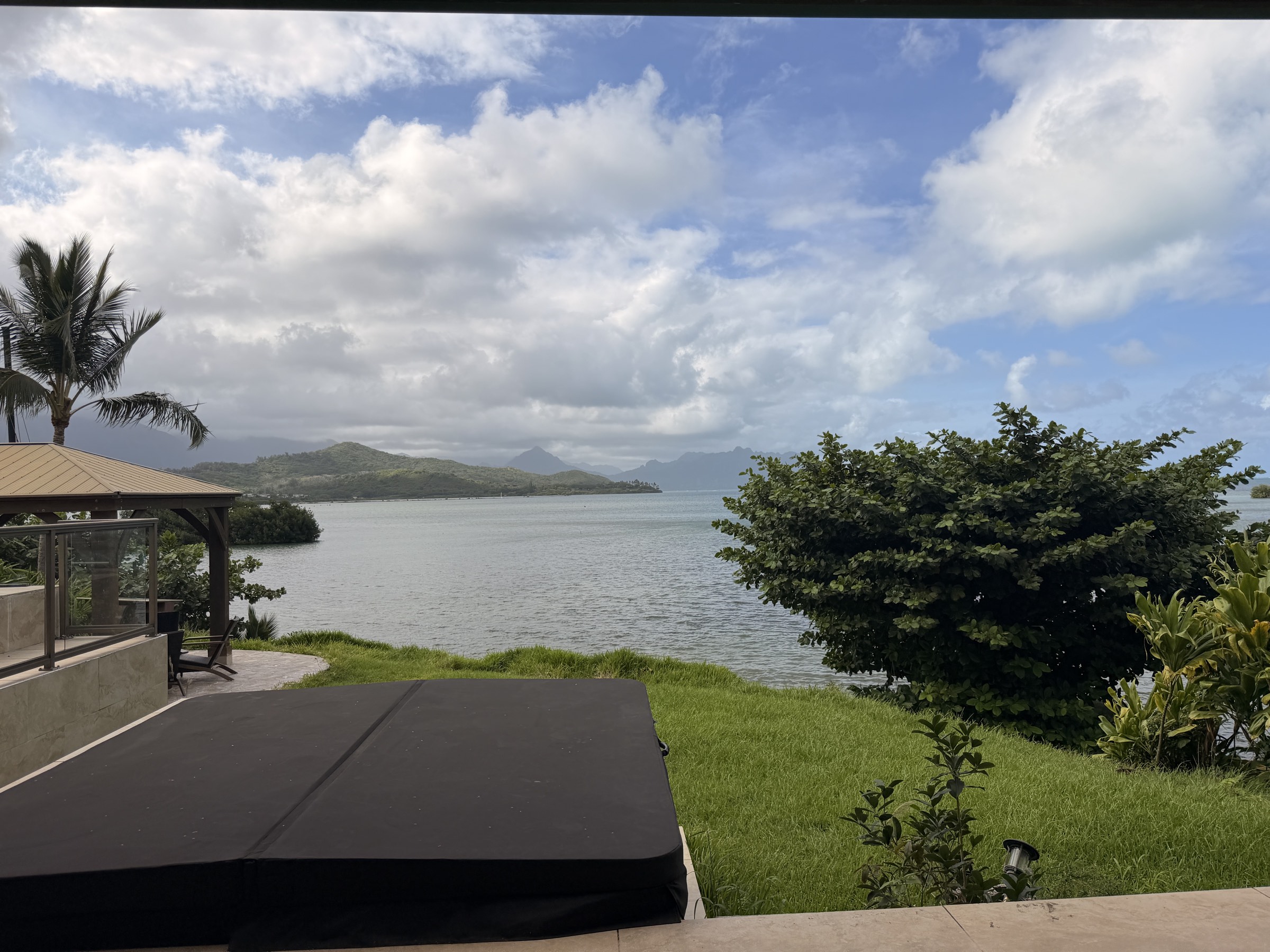 カネオヘ湾に面した家の庭。芝生の先に静かな入り江と、雲のかかったコオラウ山脈が見える。